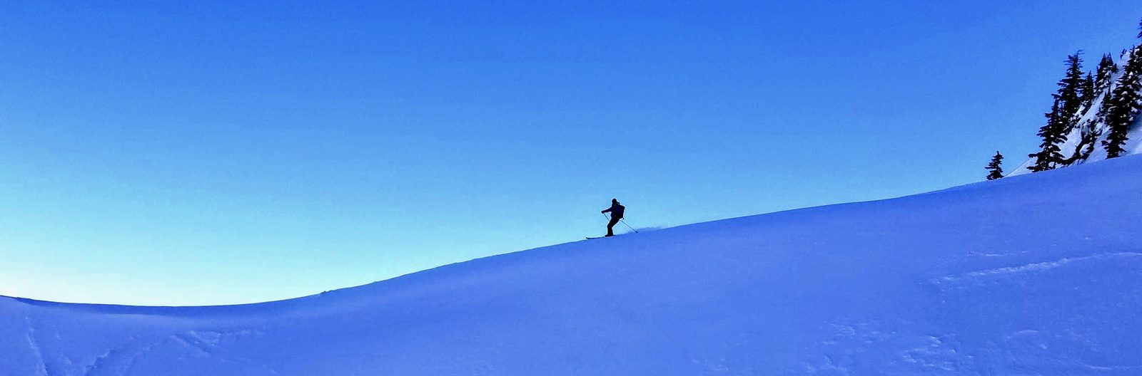 A lone skier crossing a wide open snow slope under a deep blue sky, Wonder Gully at Alpental, Washington